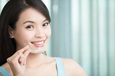 woman smiling while holding her new Invisalign clear aligners